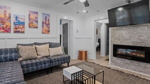 A modern living room with a sectional sofa, a glass coffee table, a fireplace, and cityscape artwork on the wall. - Charming 3-bedroom house with WiFi and AC in marvelous Atlanta (Atlanta)