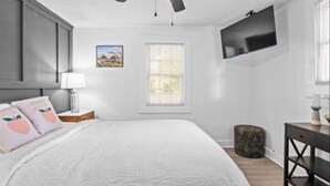 A bedroom with a bed, a ceiling fan, a TV mounted on the wall, a window, and a nightstand with a lamp. - Charming 3-bedroom house with WiFi and AC in marvelous Atlanta (Atlanta)