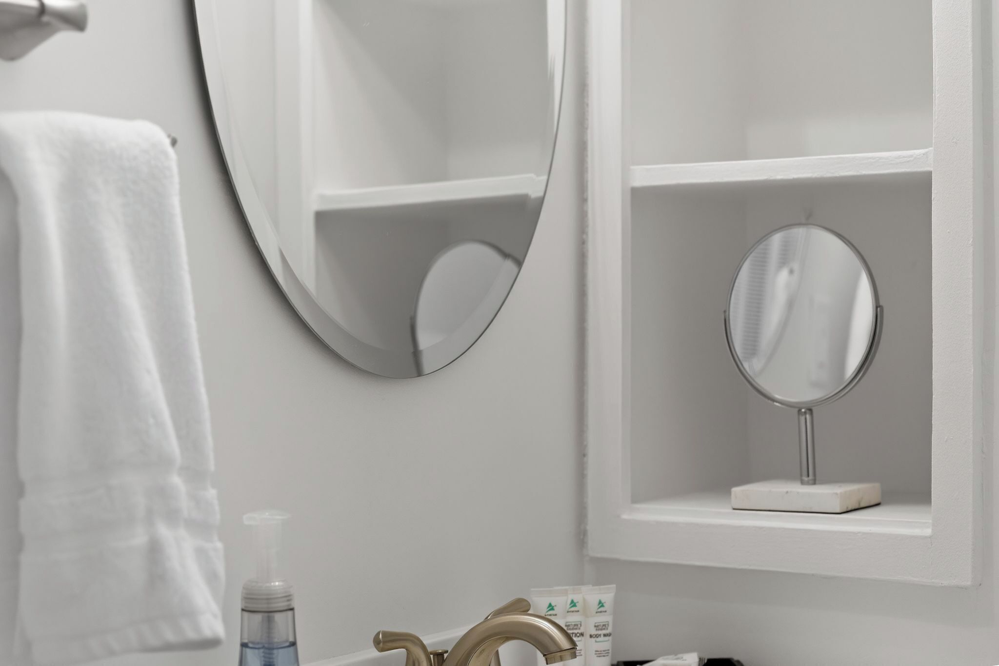A bathroom with a white sink, a mirror, a towel, and a soap dispenser.