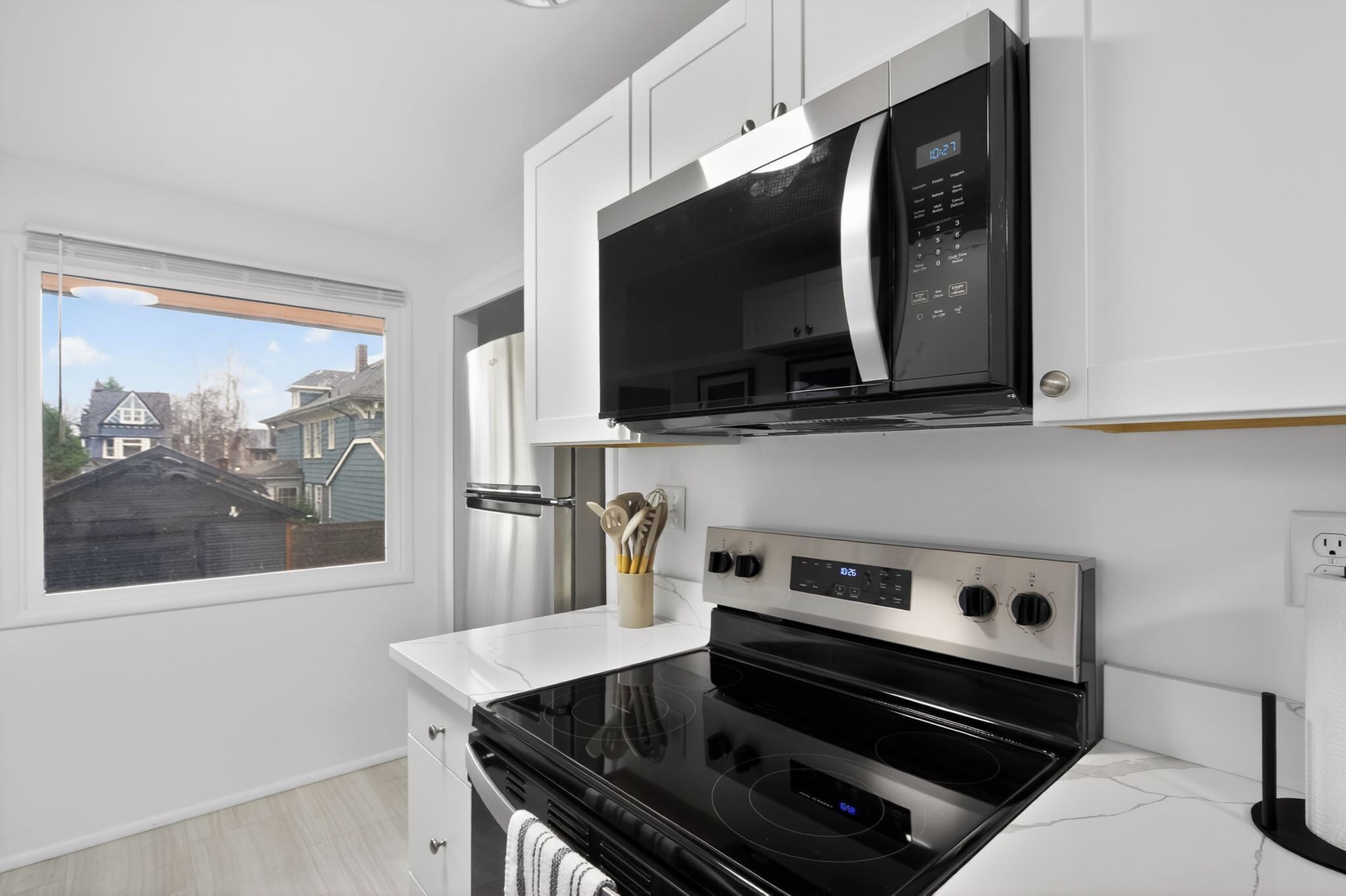A modern kitchen with a built-in microwave, oven, and a window overlooking a residential area.