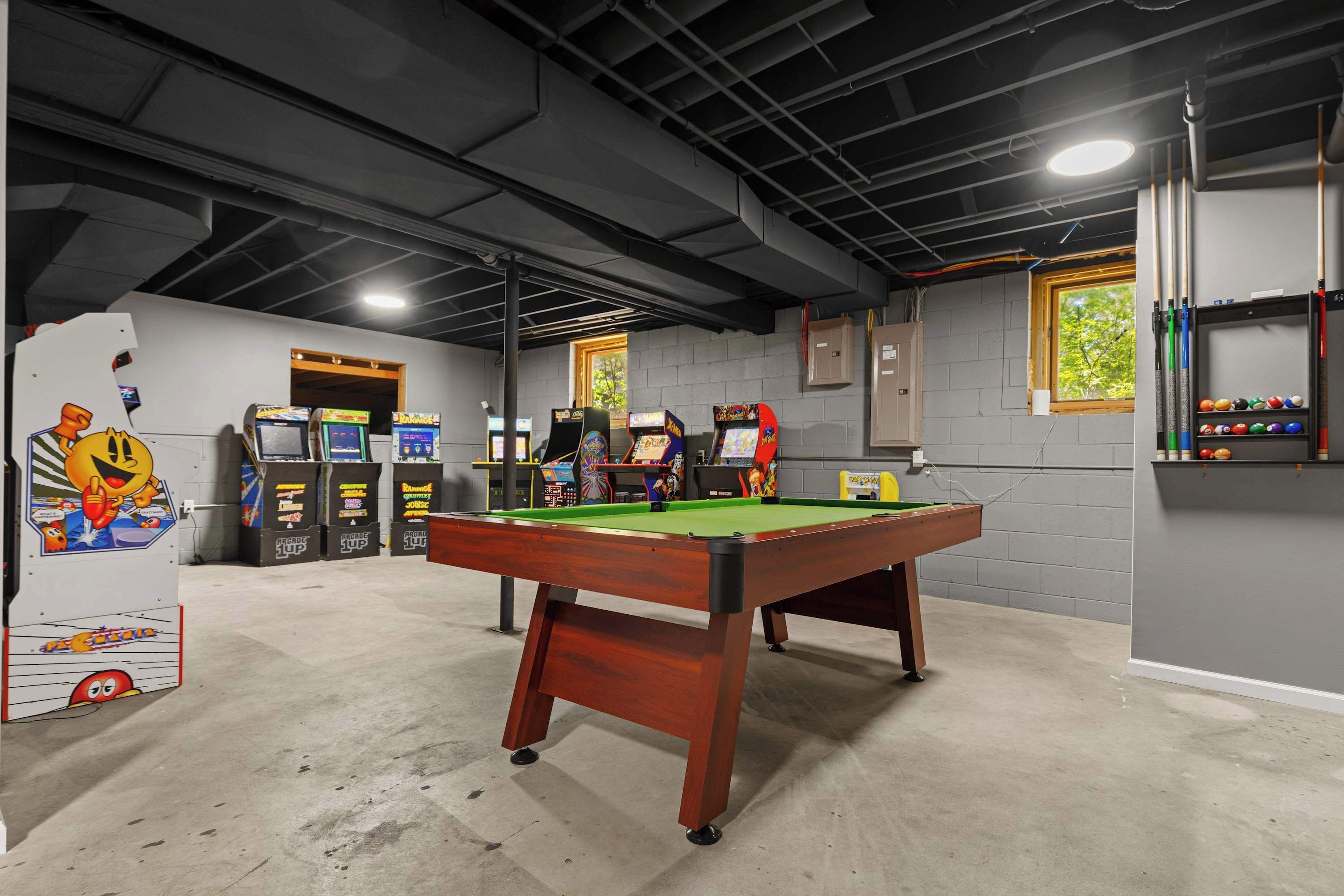A recreational room with a pool table, arcade games, and a window.