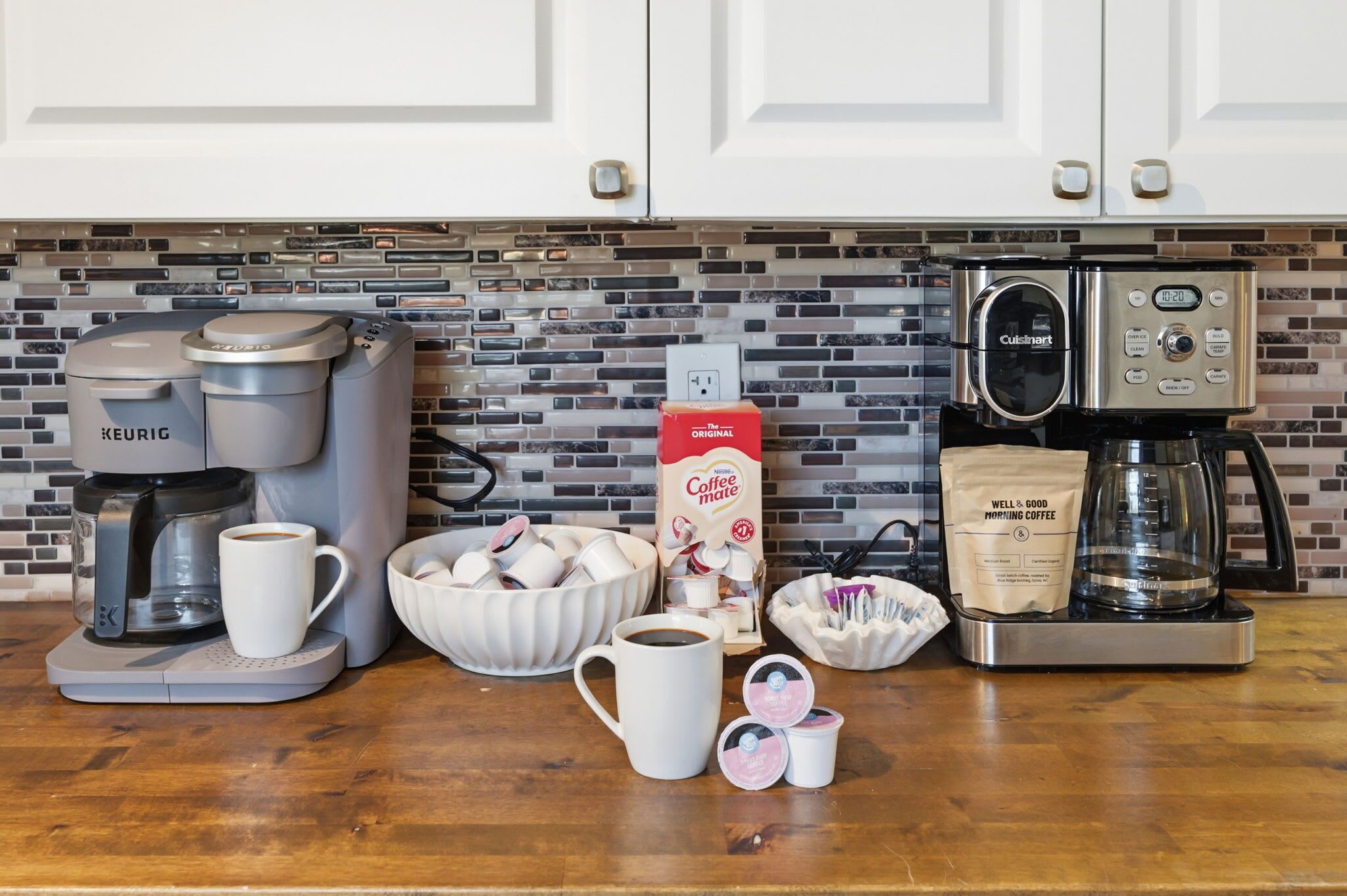 Une cuisine équipée d’une machine à café, d’une cafetière, d’un distributeur de capsules de café et d’un sac de café.