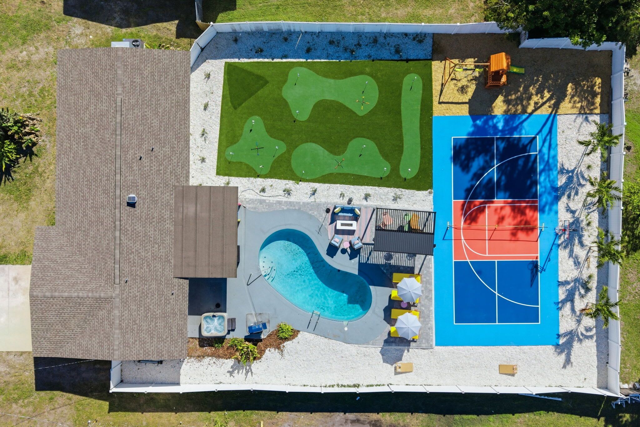 An aerial view of a backyard with a swimming pool, a basketball court, and a putting green.