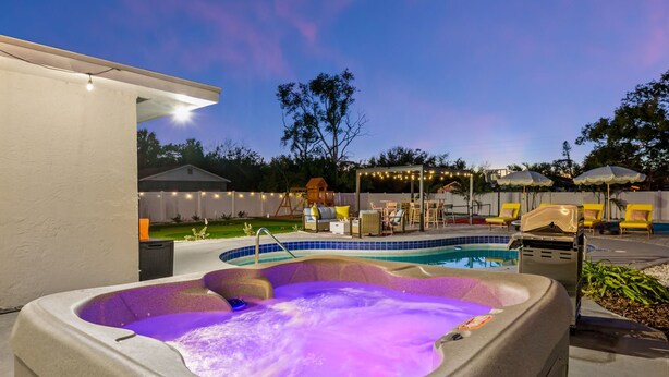 A hot tub with a purple light, a pool, outdoor seating, and string lights. - Pastel Palms | Resort Pool, Hot Tub & Sport Court (Bradenton)
