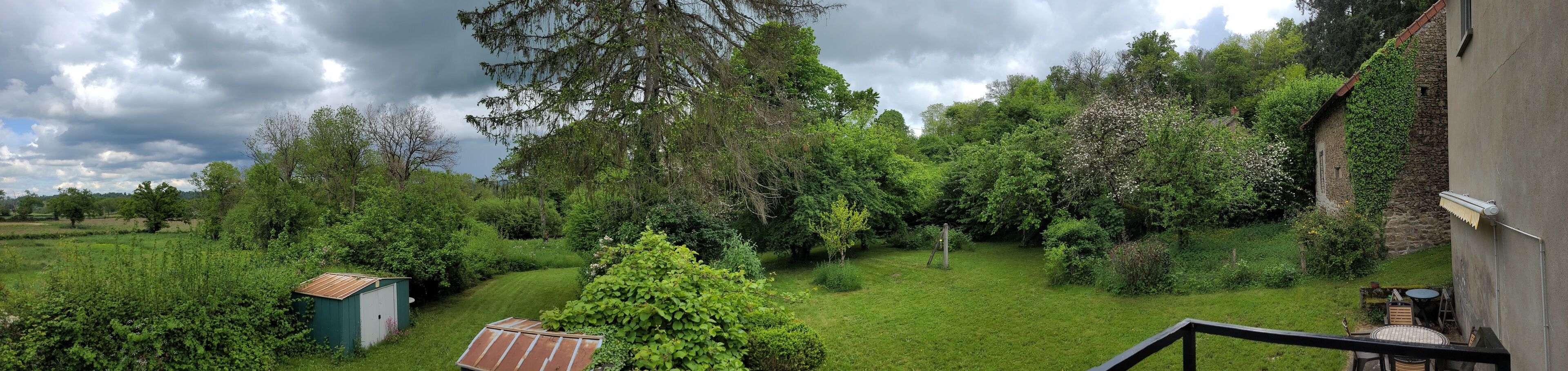 Un jardin luxuriant avec un petit abri de jardin, un banc en bois et un mur de pierre.