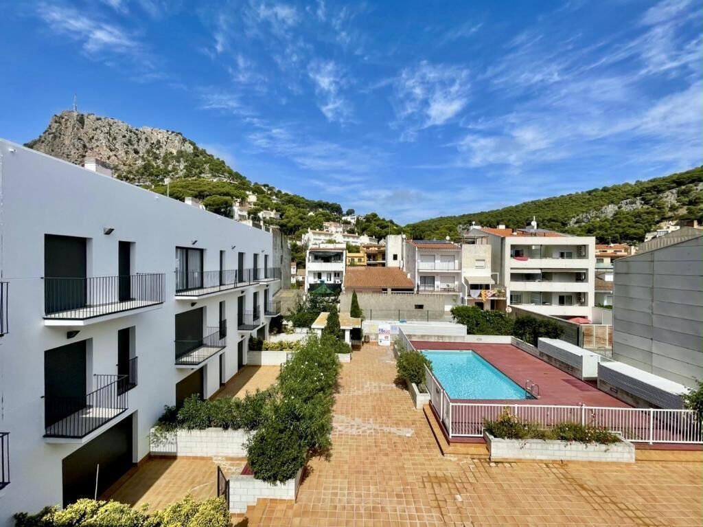 A modern building with multiple balconies, a swimming pool, and a mountainous backdrop.