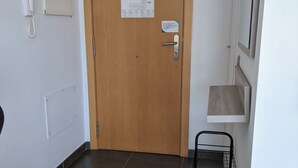 Un corridoio con una porta in legno, un telefono, una bacheca e una rastrelliera metallica.