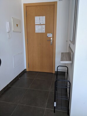 Un couloir avec une porte en bois, un téléphone, un tableau d’affichage et un présentoir en métal.