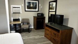 A hotel room with a bed, a desk with a computer, a chair, a television, a dresser, and a microwave. - Cozy Queen Room on Main Street in Longmont (Longmont)
