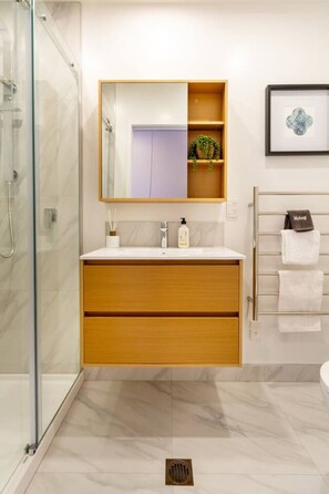 Een moderne badkamer met een glazen douchecabine, een houten wastafelmeubel met een spiegel en een handdoekrek.