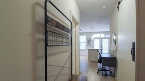 A hallway with a metal rack, a desk with a chair, and a window with blinds. - Refresh Tanglewood Spacious 1BR in Uptown Houston (Houston)