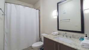 A bathroom with a shower curtain, toilet, sink with a mirror, and a towel rack. - Refresh Tanglewood Spacious 1BR in Uptown Houston (Houston)
