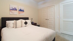 A bedroom with a bed, two wall-mounted paintings, a ceiling fan, a nightstand, and a white door. - Refresh Tanglewood Spacious 1BR in Uptown Houston (Houston)