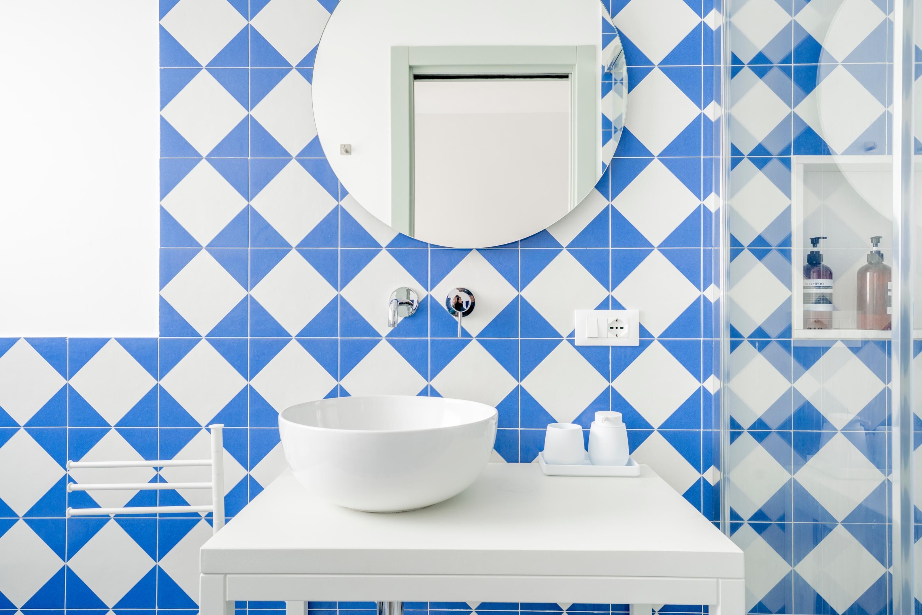 Une salle de bain avec un lavabo blanc, un miroir et des carreaux bleus à motifs losangés.