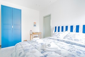 Quarto com cama, um guarda-roupa azul, uma mesinha de cabeceira com abajur e uma porta.