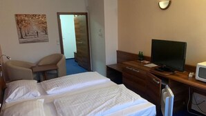 Hotellihuone, jossa on sänky, työpöytä, jossa on tietokone ja televisio, tuoli ja taulu seinällä.