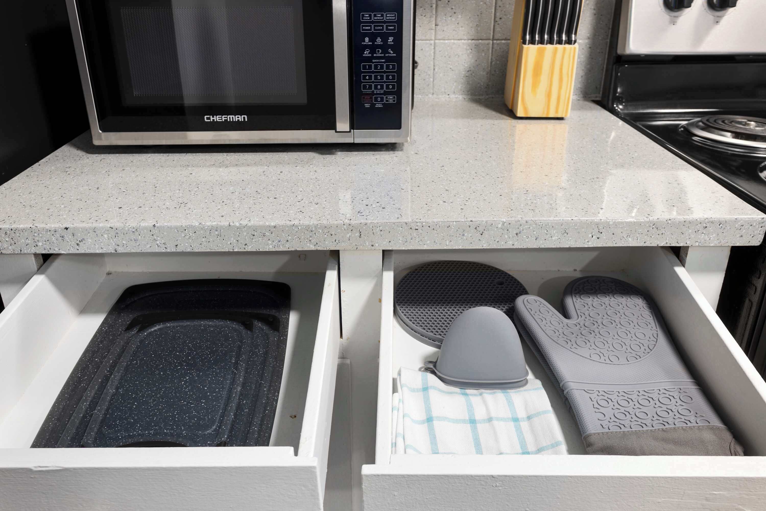 Una cocina con microondas, estufa y un cajón que contiene una espátula y un paño.