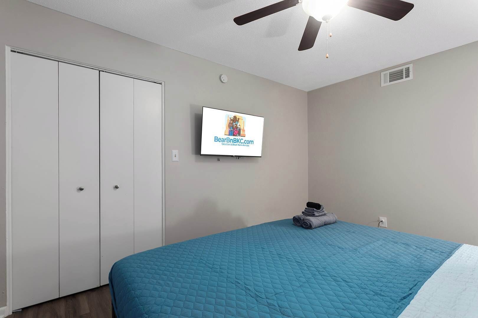 A bedroom with a bed, a ceiling fan, a TV mounted on the wall, and a wardrobe.