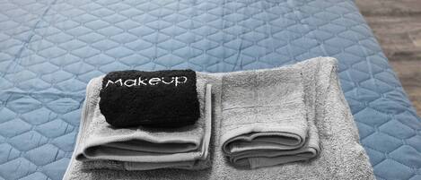 A bed with a quilted blue cover and a folded grey towel with a black tag labeled "makeup".