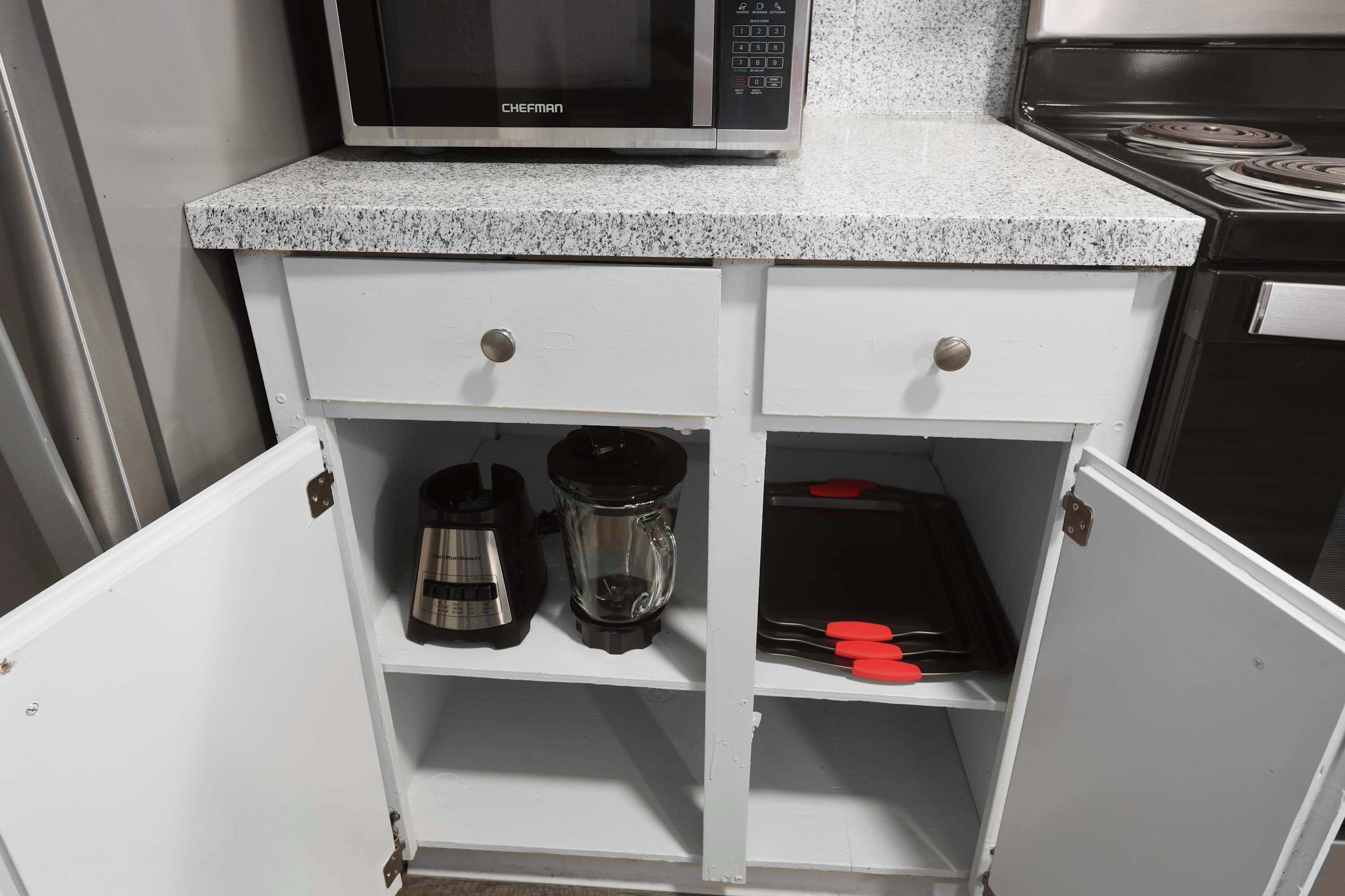 Et køkken med en mikrobølgeovn på bordpladen, en kaffemaskine og en blender på nederste hylde.