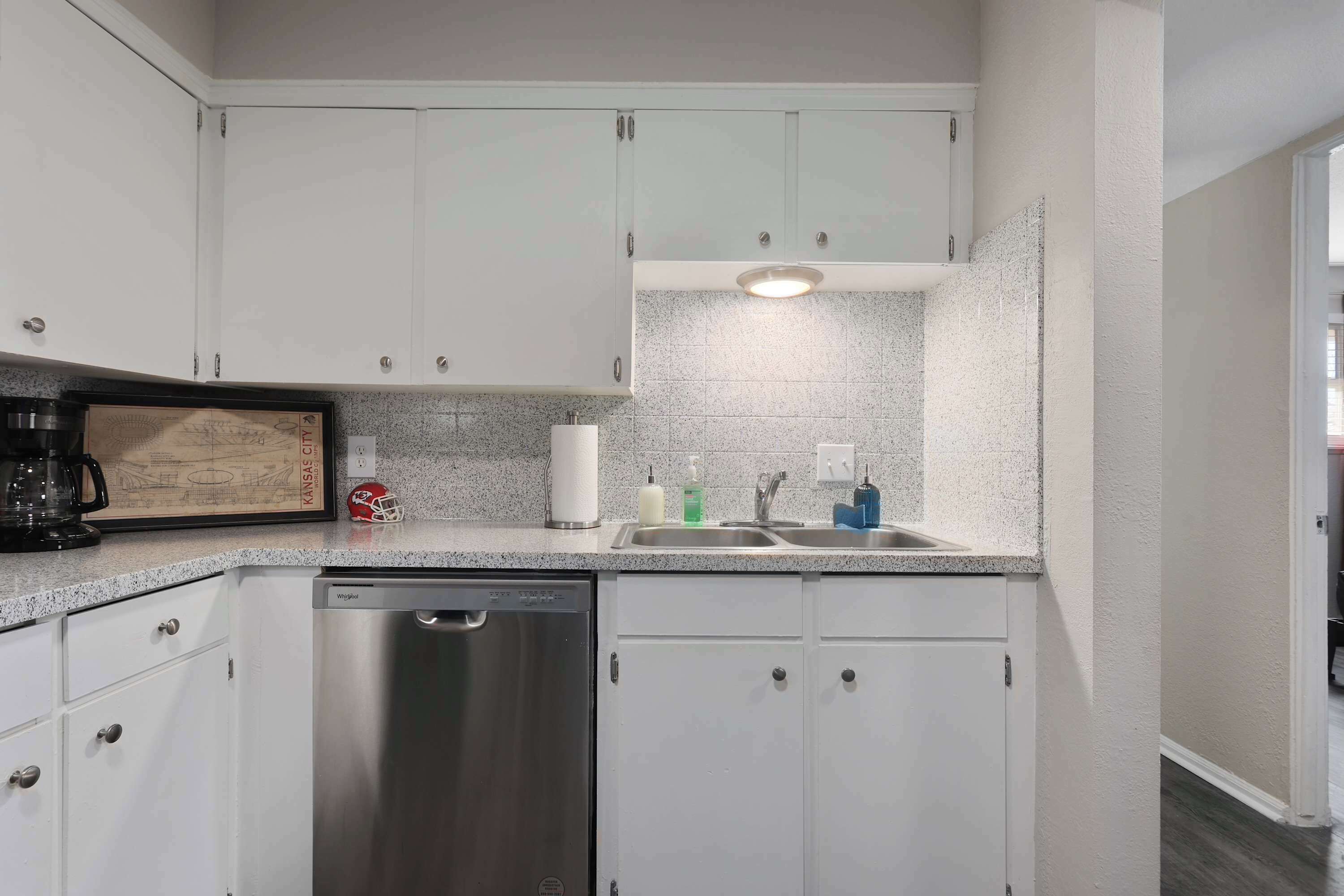A kitchen with white cabinets, a stainless steel dishwasher, a granite countertop, and a framed picture on the counter.