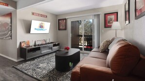 A modern living room with a flat-screen TV, a sofa, a coffee table, and a sliding glass door leading to an outdoor area. - Chief Themed 2 BR APT_KingBeds_Near Dining (Kansas City)