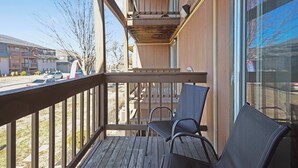 A balcony with wooden railings, a chair, and a view of a parking lot and buildings. - Chief Themed 2 BR APT_KingBeds_Near Dining (Kansas City)