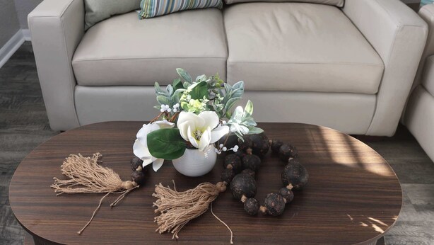 Une table basse ronde en bois, sur laquelle se trouve un vase blanc contenant des fleurs et une guirlande de perles.