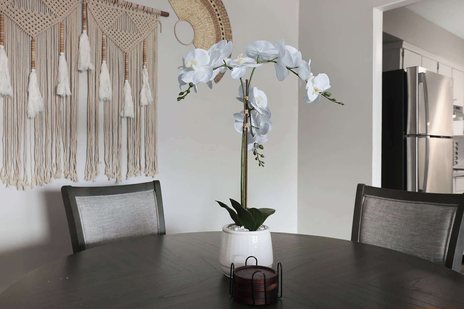 A dining table with a white orchid in a ceramic pot, surrounded by chairs.