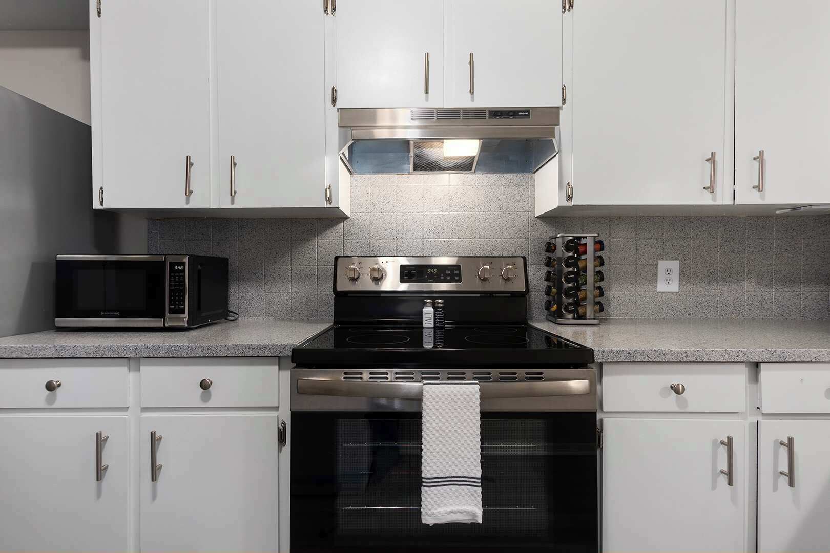 Una cocina con armarios blancos, una estufa negra, un microondas y una estantería para vinos.