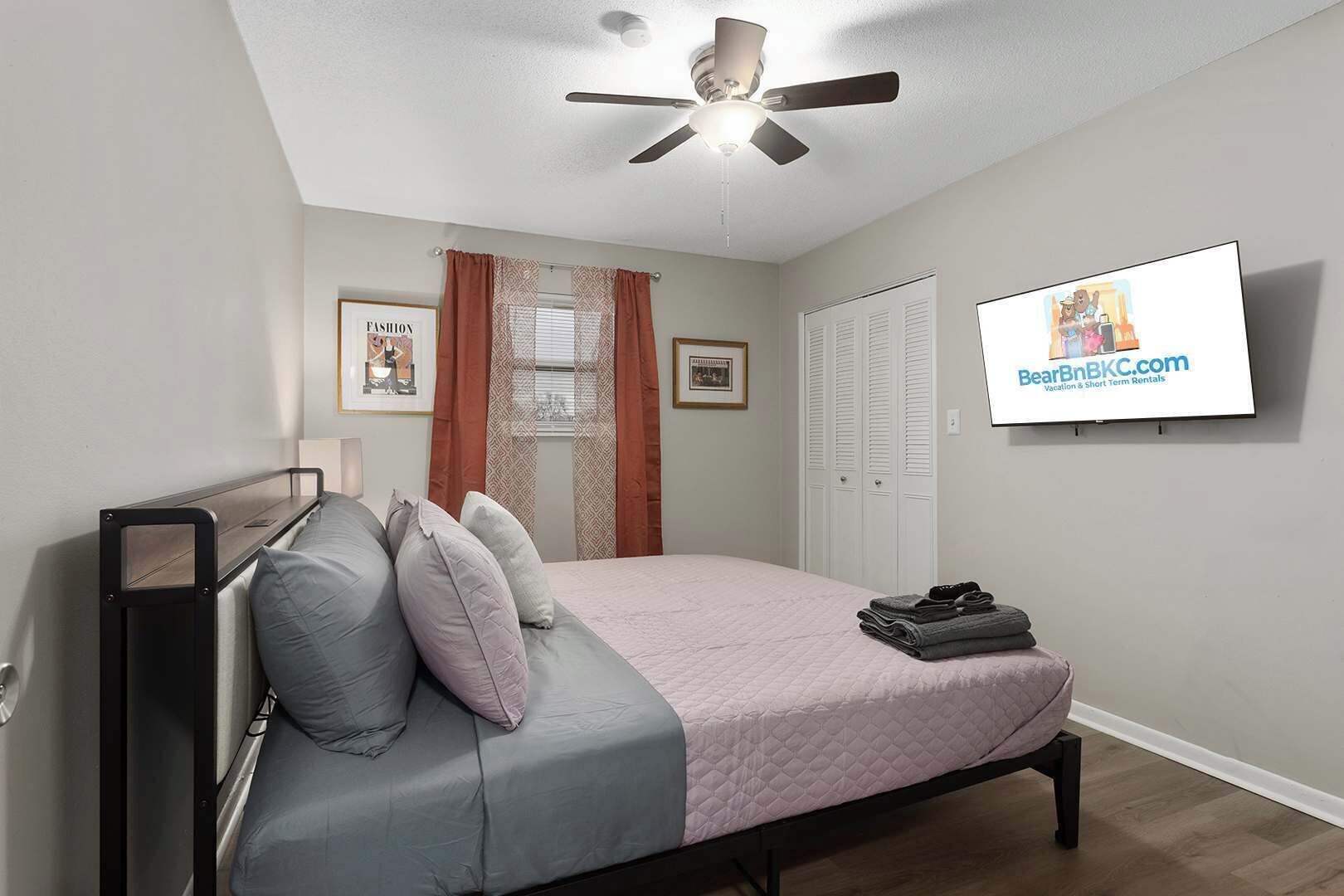 A bedroom with a bed, a ceiling fan, a TV, and a wardrobe.
