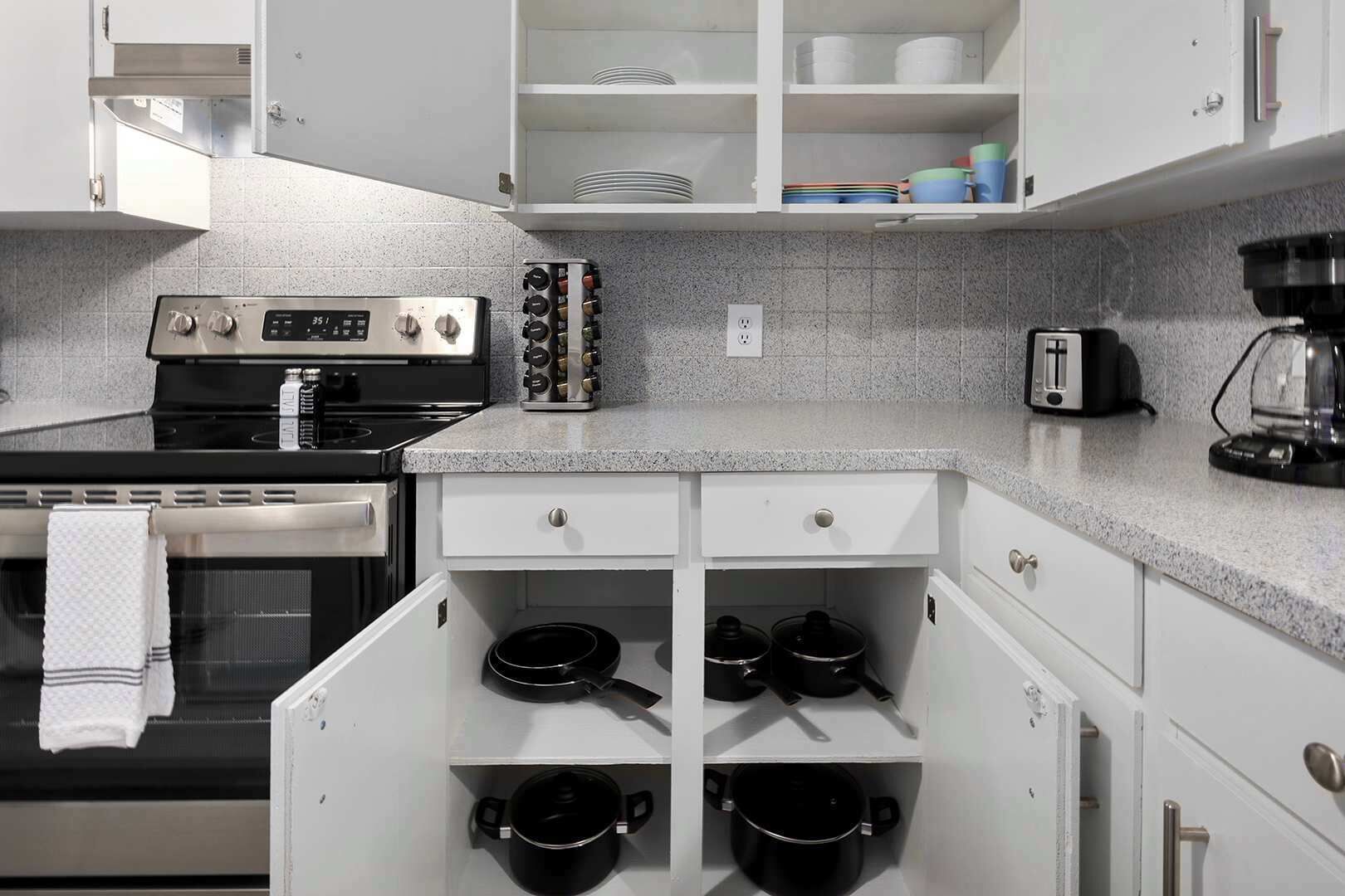 A kitchen with white cabinets, a stove, a coffee maker, and black pots.