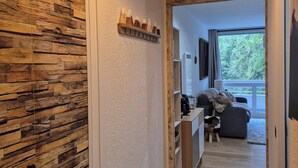 En gang med trævæg, en hængende lampe, et knagered og udsigt til en stue med sofa og vindue.