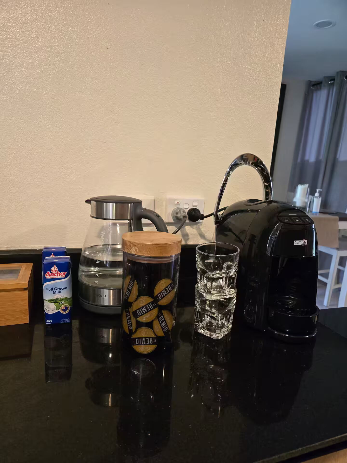 Un comptoir de cuisine avec une machine à café, une tasse, un carton de lait et une bouteille d’eau.