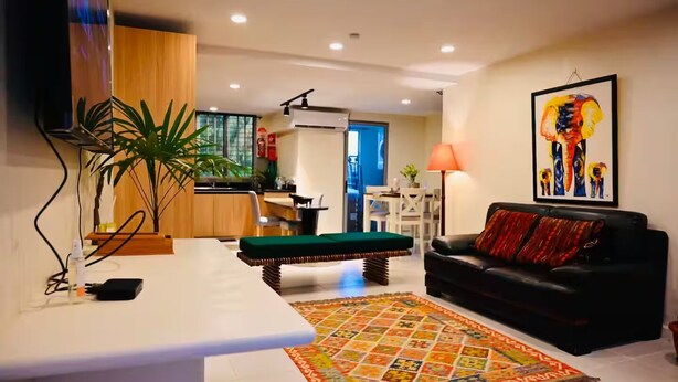 A modern living room with a black leather sofa, a green ottoman, and a colorful rug. - Lavish Lodge (Suva)