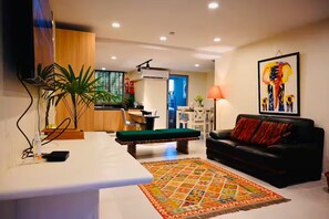 A modern living room with a black leather sofa, a green ottoman, and a colorful rug.