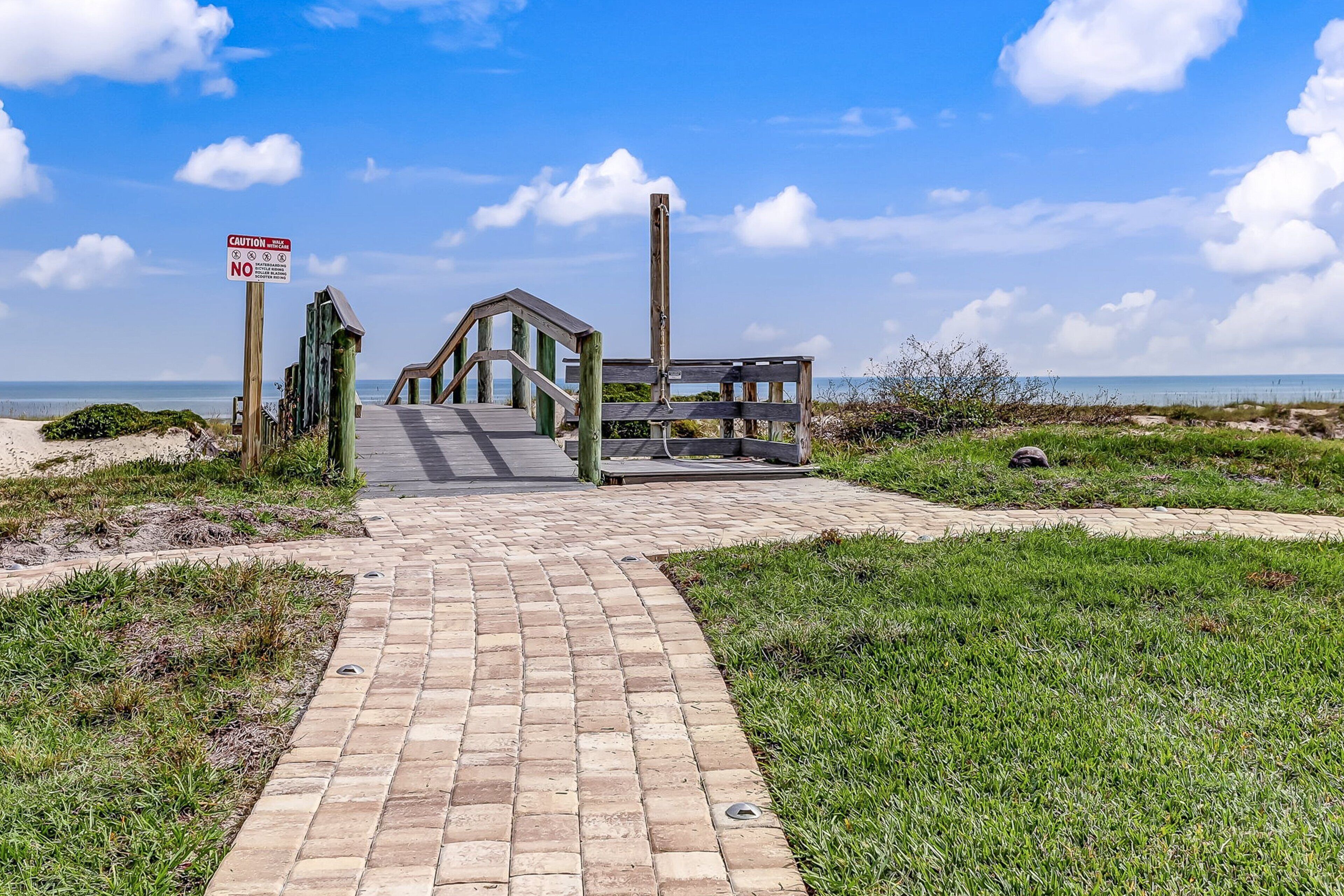 A wooden boardwalk leading to a beach with a caution sign.