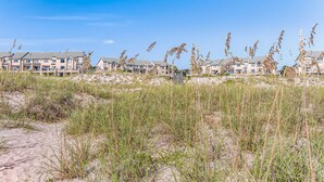 Un hotel sulla spiaggia con edifici a più piani, dune sabbiose e alte graminacee.