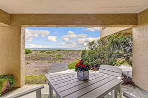 A covered patio with a table and chairs, a flower vase, and a view of the ocean and landscape. - Beachfront Condo With Outdoor Pool, Patio & Washer/dryer - Dog-friendly (Fernandina Beach)