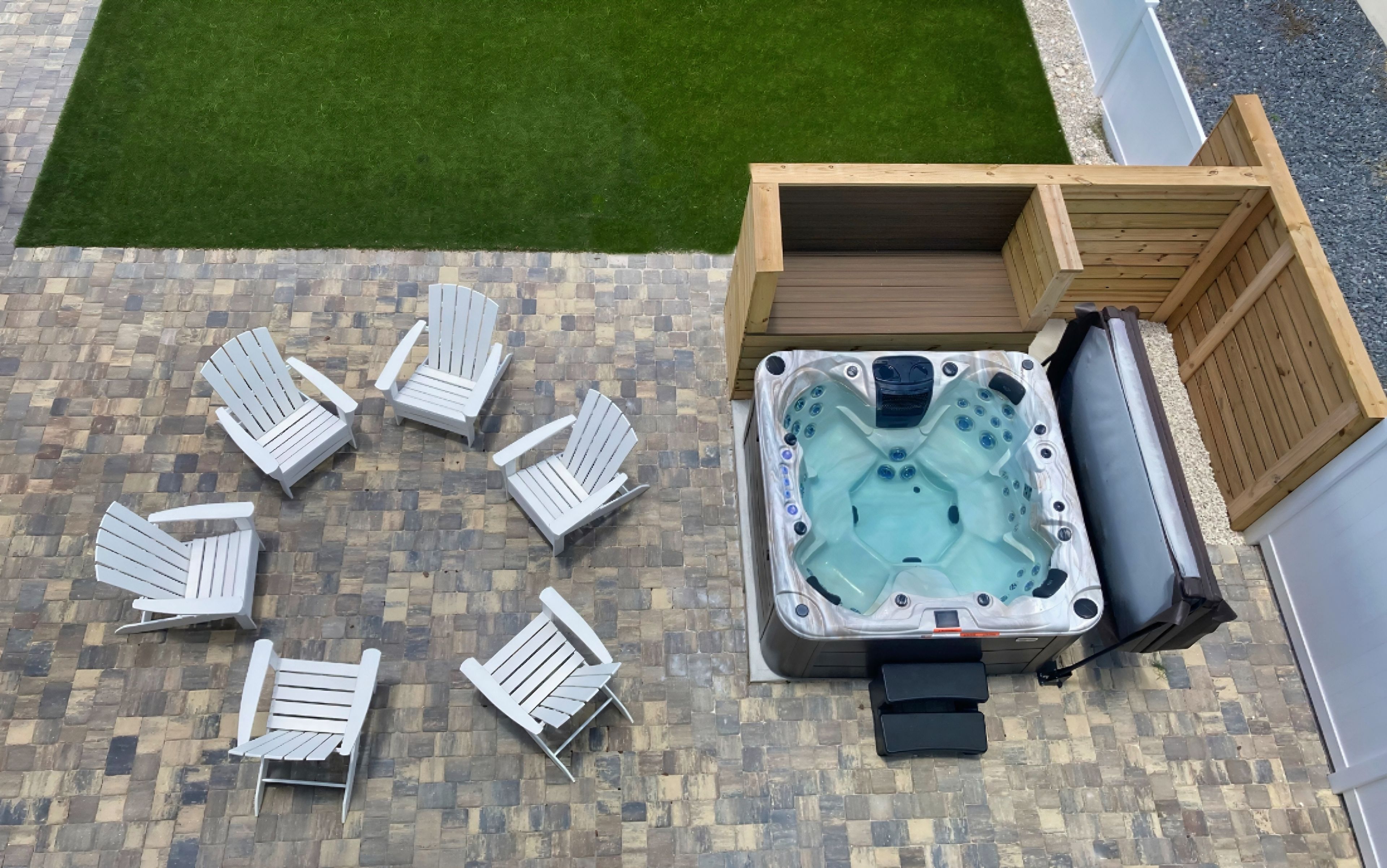 Een hottub met een houten terras en zes Adirondack-stoelen eromheen.