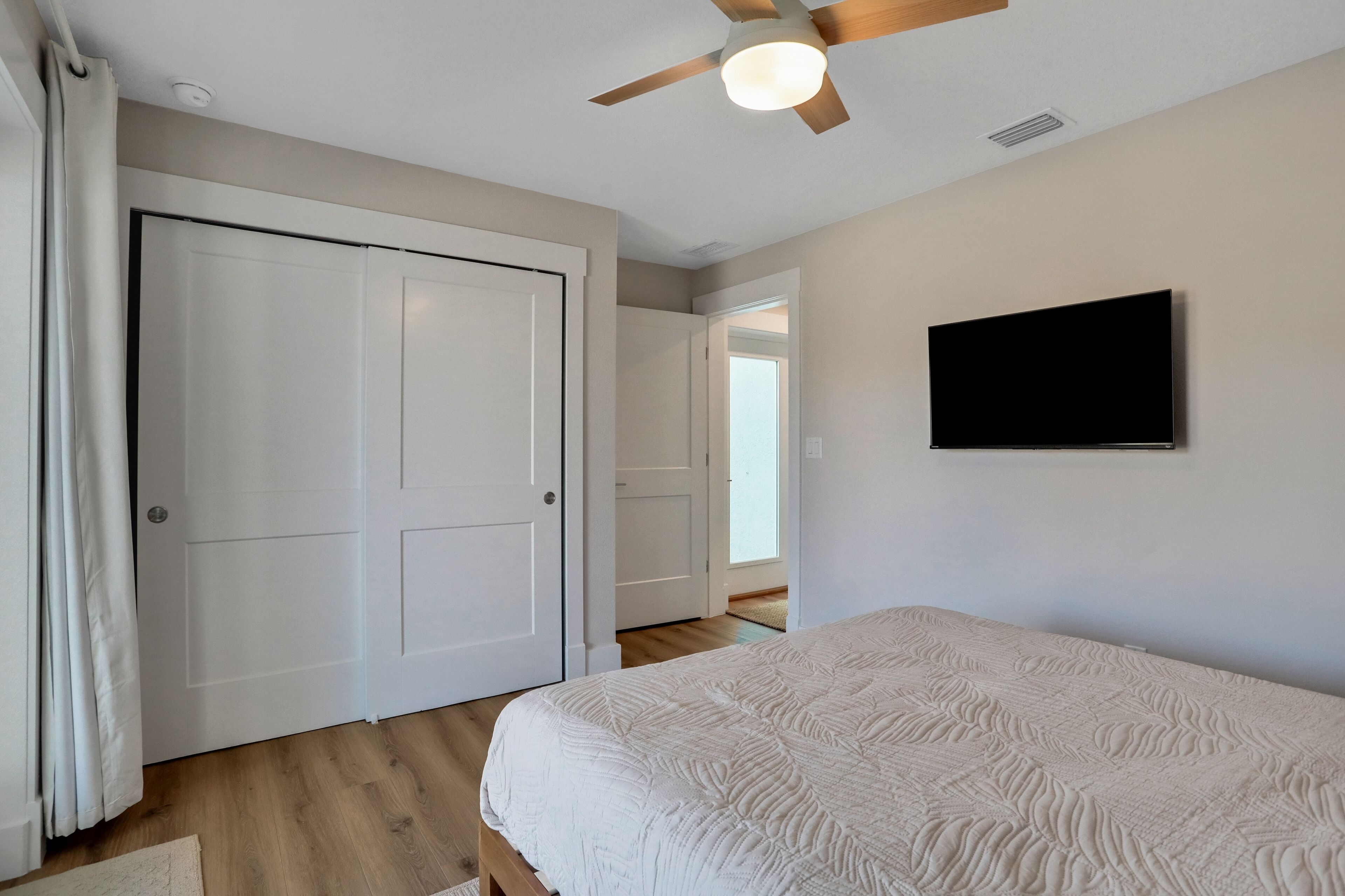 Un dormitorio con cama, ventilador de techo, televisor y una puerta.