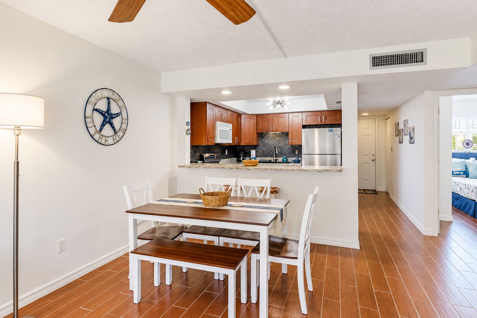 A modern kitchen with wooden cabinets, a stainless steel refrigerator, and a dining area with a wooden table and white chairs.