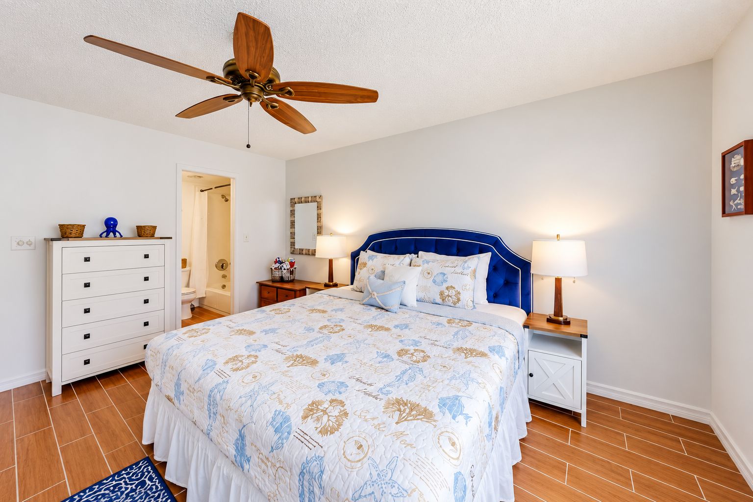 A bedroom with a bed, a dresser, a nightstand, a ceiling fan, and a bathroom door.