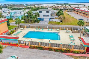 Area piscina con lettini e terrazza recintata, circondata da edifici residenziali e una spiaggia sullo sfondo.