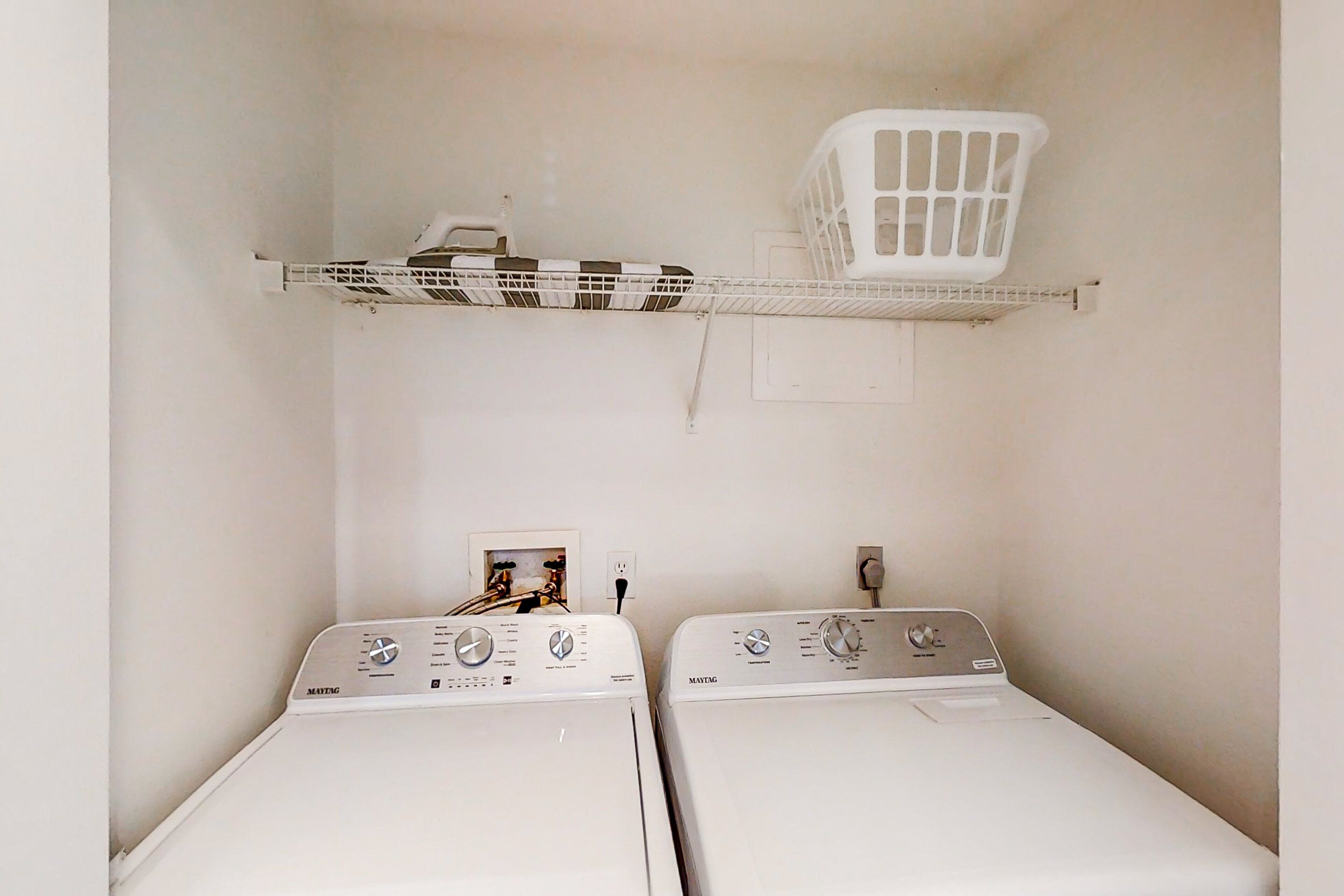 Une buanderie équipée de deux machines à laver à chargement frontal et d’un panier à linge blanc posé sur une étagère.