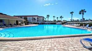 A swimming pool with lounge chairs and palm trees. - Cool Waves Oceanfront Retreat - St Augustine Beach 2 Pools 5 Hot Tubs! On the Beach (St. Augustine)
