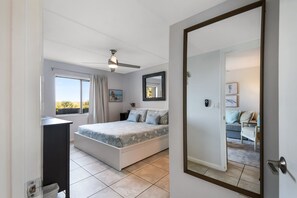 A bedroom with a bed, a desk, a ceiling fan, a window with curtains, and a view of the outdoors. - Cool Waves Oceanfront Retreat - St Augustine Beach 2 Pools 5 Hot Tubs! On the Beach (St. Augustine)