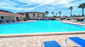 A swimming pool with lounge chairs and palm trees in the background. - Cool Waves Oceanfront Retreat - St Augustine Beach 2 Pools 5 Hot Tubs! On the Beach (St. Augustine)
