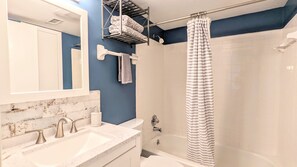 A bathroom with a white sink, two faucets, a mirror, a towel rack, a shower curtain, and a bathtub. - Cool Waves Oceanfront Retreat - St Augustine Beach 2 Pools 5 Hot Tubs! On the Beach (St. Augustine)
