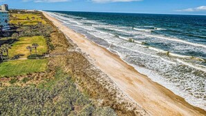 A coastal hotel with a beach view, a golf course, and a large building on the left. - Dog-friendly Condo on the Golf Course With Ocean View, Pools, gym & Beach Access (Palm Coast)